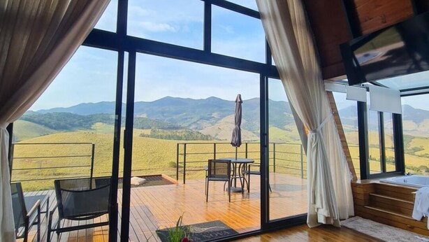Il s'agit d'une pièce spacieuse dotée de grandes fenêtres qui offrent une vue sur des collines verdoyantes. À l'extérieur, on trouve une terrasse en bois avec une table et des chaises.