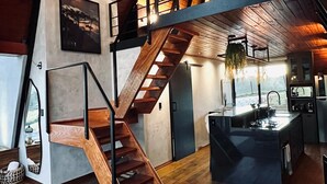 Ein modernes Interieur mit einer Holztreppe, einer Küchenzeile und einer Sitzecke mit Sofa und Dekoration.