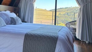 Une chambre avec une grande fenêtre, un lit et une vue sur un paysage vallonné.