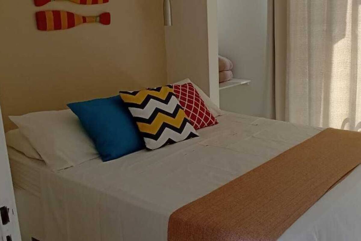 A neatly made bed with a white comforter, a brown throw blanket, and two decorative pillows.