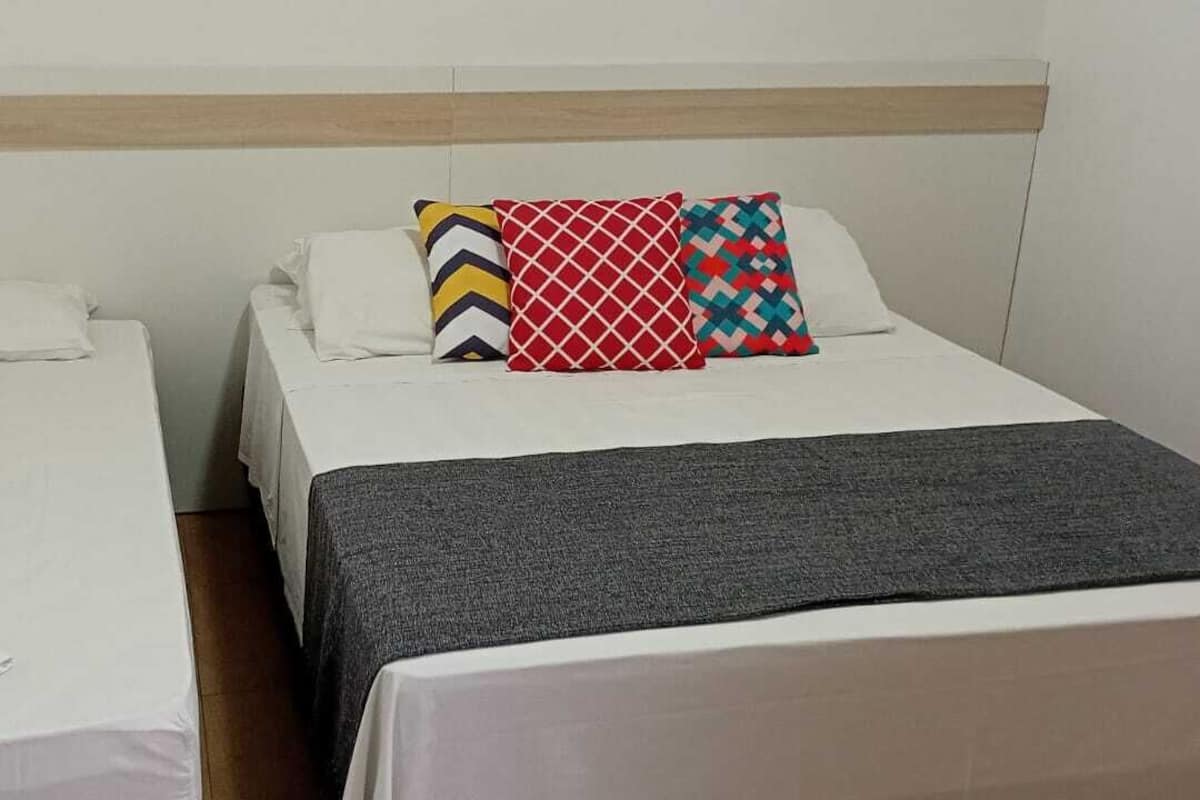 Two single beds with white linens, a grey blanket on the right bed, and colorful pillows on the left bed.