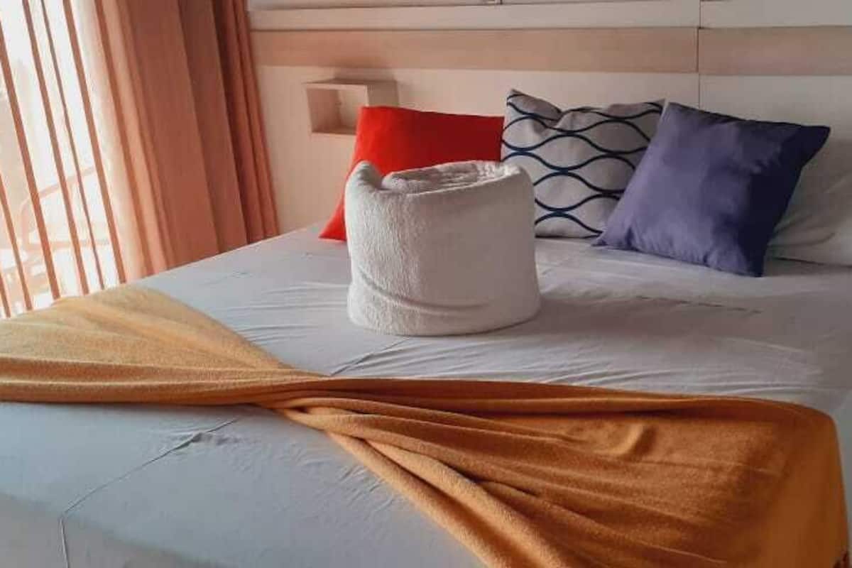 A bed with a white headboard, a white blanket, and a brown throw. There are pillows in red, blue, and white.