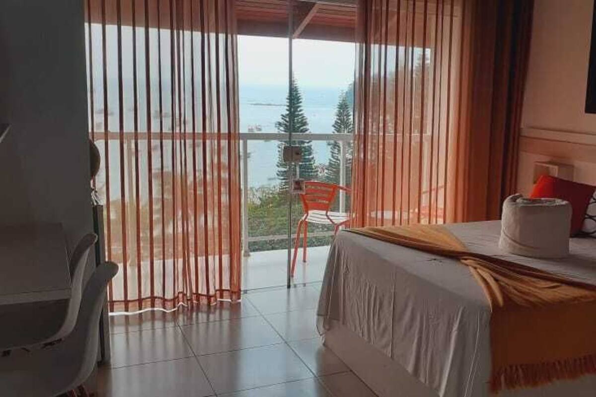 A bedroom with a bed, a chair, and a view of the sea through large windows.