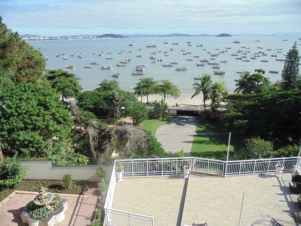 A coastal view with numerous boats on the water, a beach, and a garden area with a fountain. - Maricá Apart Hotel (Penha)