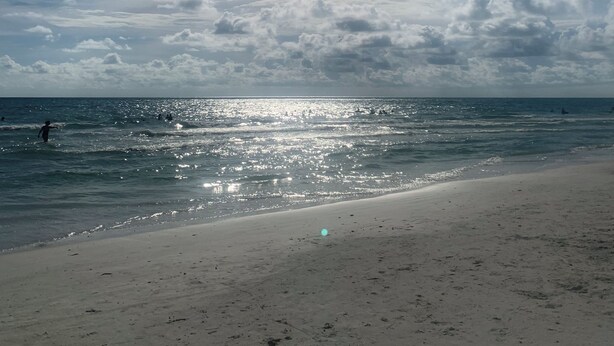 Una playa con cielo despejado y luz del sol reflejada en el agua.