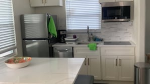Una cocina moderna con armarios blancos, un refrigerador de acero inoxidable, un microondas y un ventilador de techo.
