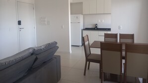 Uma sala de estar moderna com sofá, mesa de jantar e cadeiras, e área de cozinha ao fundo.