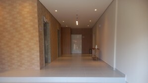 Um corredor limpo e moderno com piso ladrilhado, um banco de madeira e uma pequena mesa com um vaso.