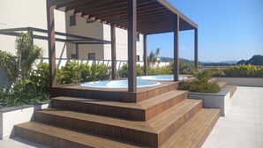 Área de piscina no terraço com escadas de madeira para um ofurô, rodeado por plantas em vasos e vista desobstruída das montanhas.