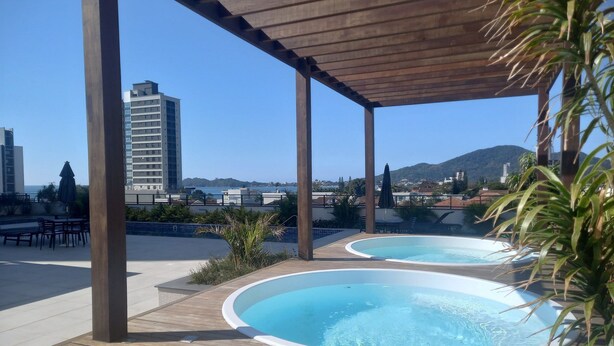 Área de piscina no terraço com duas banheiras de hidromassagem, deck de madeira e vista para a cidade e montanhas.