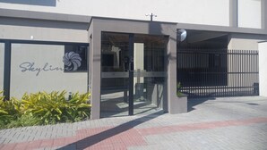 Um edifício moderno com entrada de vidro, uma placa com a inscrição "Skyline" e uma área de estacionamento murada.