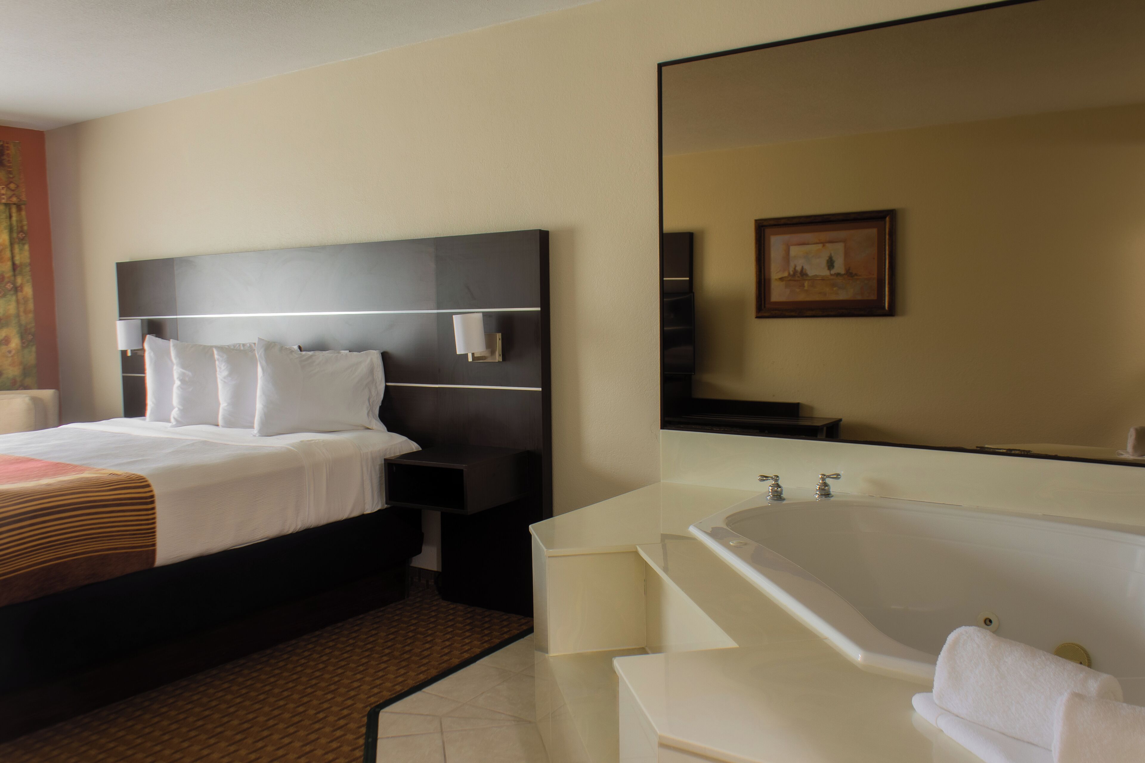 A hotel room with a bed, bedside table, nightstand, and a large mirror.