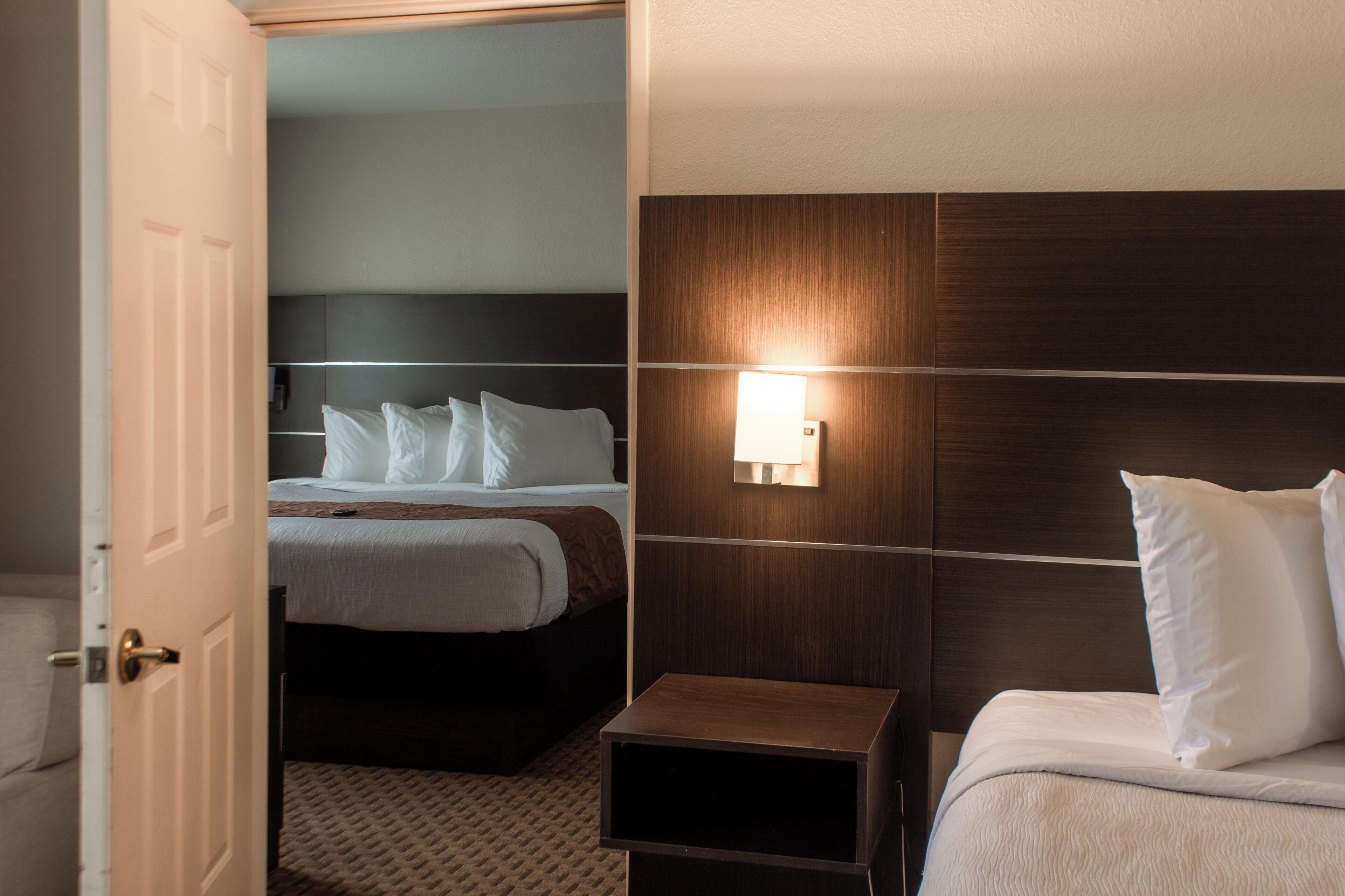 A hotel room with a bed, a bedside table, a nightstand, and a wall-mounted light fixture.