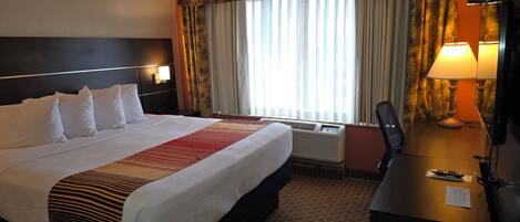 A hotel room with a large bed, a desk with a lamp, and a window with curtains.