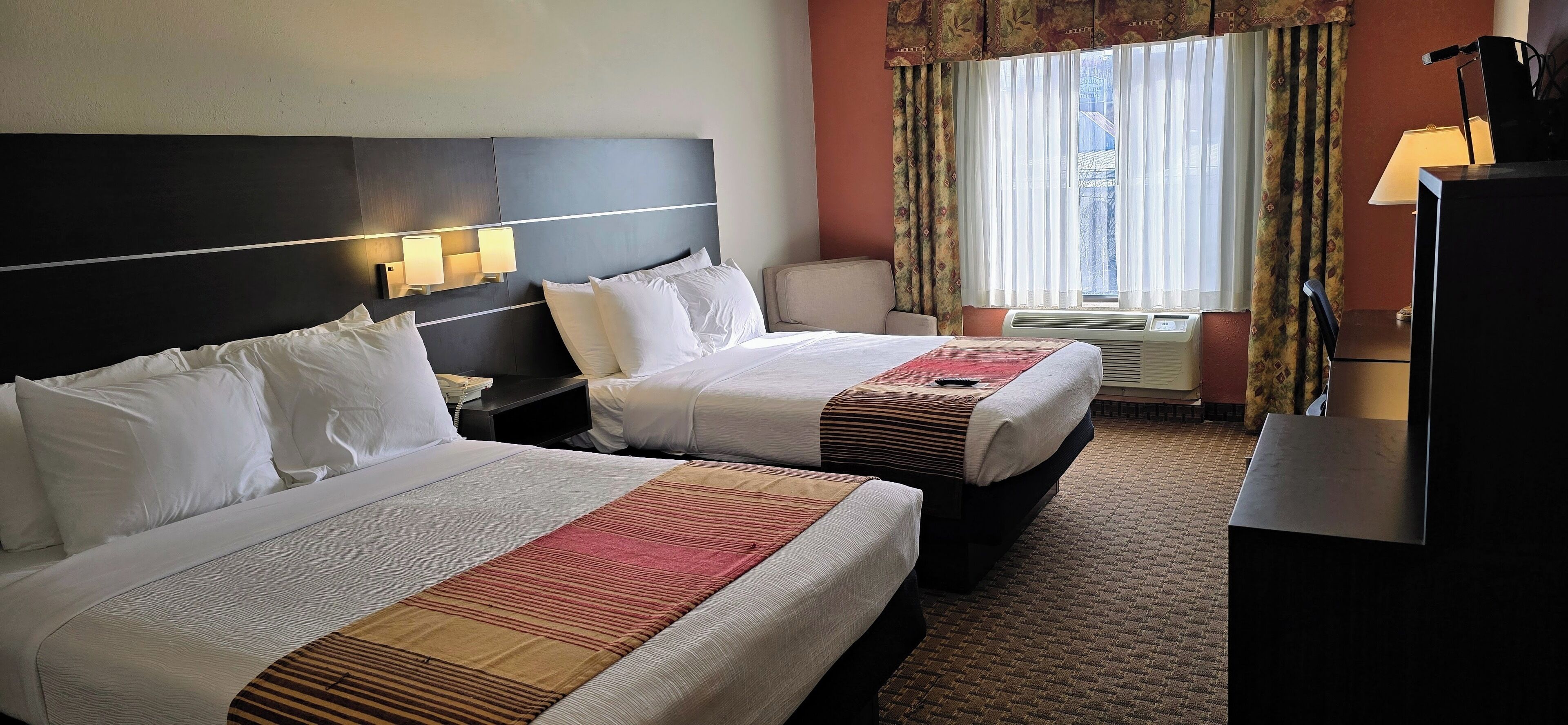 Une chambre d’hôtel avec deux lits, un bureau, une lampe et une fenêtre avec des rideaux.