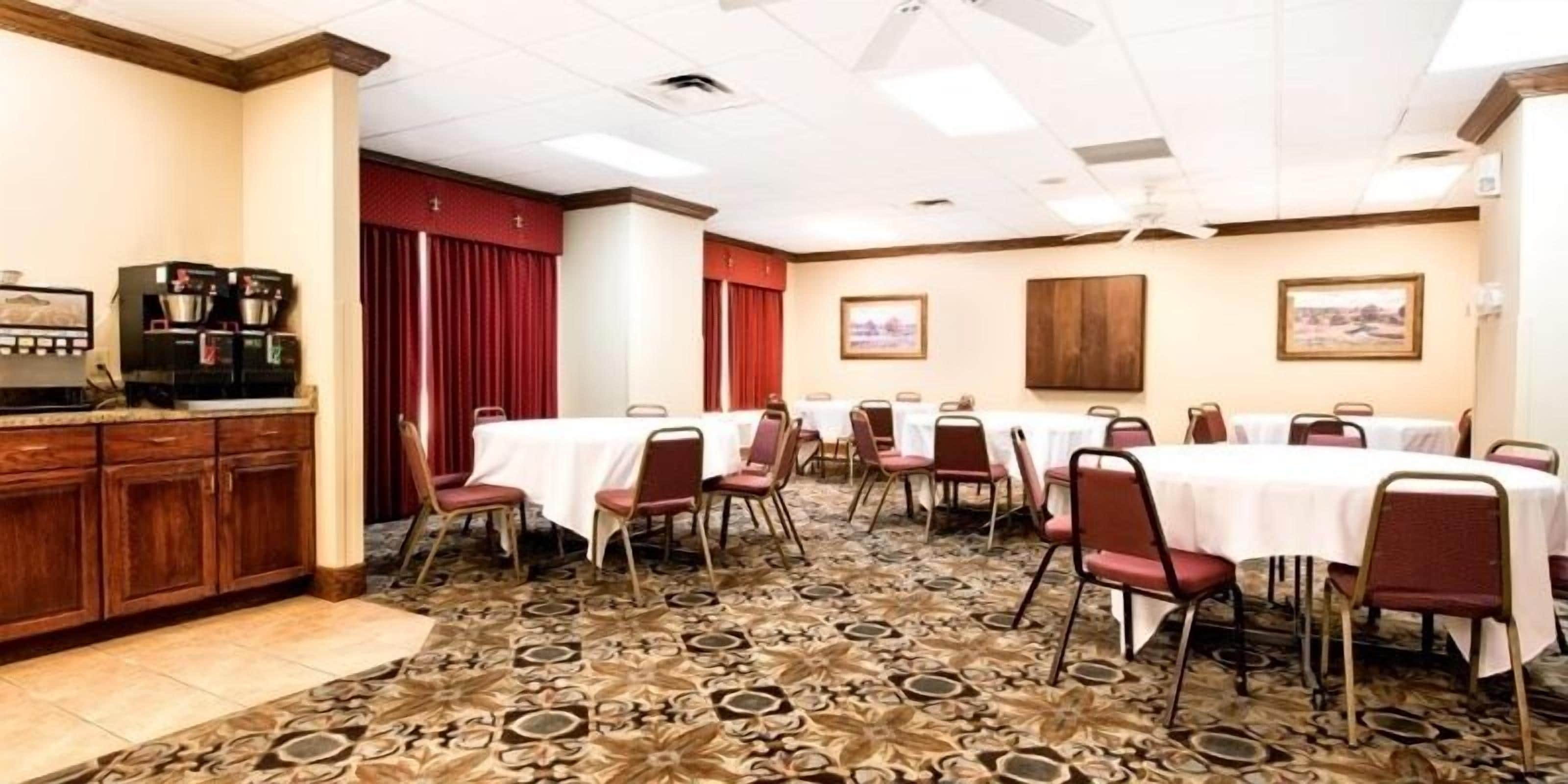 A conference room with multiple tables and chairs, a coffee machine, and patterned carpet.