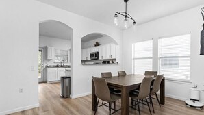 Une cuisine moderne avec des meubles blancs, une table à manger entourée de six chaises et un luminaire au plafond.