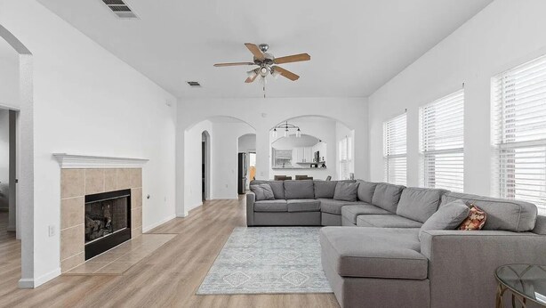 Un salon spacieux avec un canapé d’angle, une cheminée et un ventilateur de plafond.