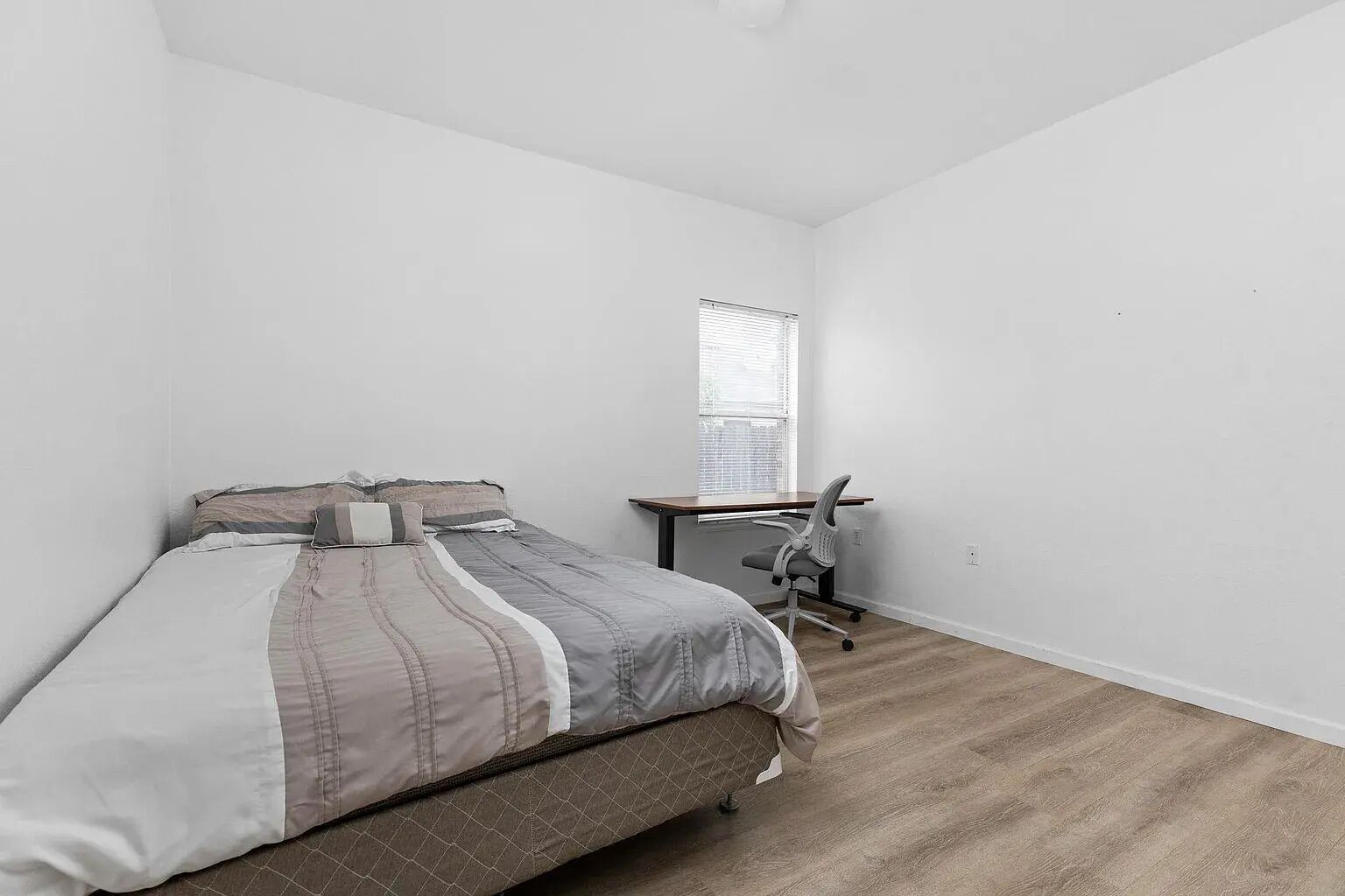 A small, sparsely furnished room with a bed, a desk, and a window.