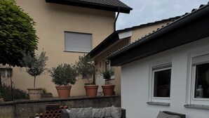An outdoor patio with wicker furniture, potted plants, and a building in the background.