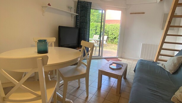 A room with a dining table, chairs, a TV, a sofa, and a staircase. - Small house Hourtin port (Hourtin)