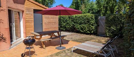 Un jardin avec un barbecue, une table de pique-nique et des chaises longues.