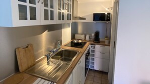 A compact kitchen with white cabinets, a stainless steel sink, a microwave, and a toaster. - Small house Hourtin port (Hourtin)