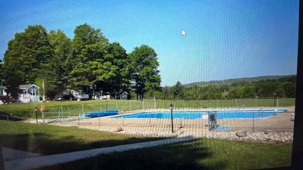 Vista de una zona de piscina con cielo despejado, rodeada de árboles y una cerca.