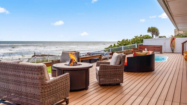 Eine Holzterrasse mit Korbmöbeln, einem Feuerkorb und Blick auf das Meer.
