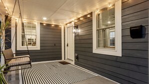 Une véranda couverte avec un tapis rayé noir et blanc, un fauteuil suspendu et des guirlandes lumineuses.