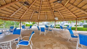 An outdoor patio with thatched roof, blue chairs, and tables.