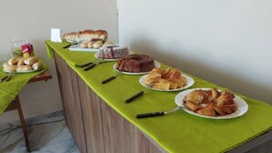 Una mesa de buffet con varios productos de panadería y un pastel, sobre un mantel verde.