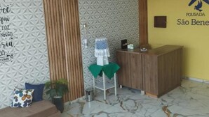 Un área de recepción con un mostrador de madera, una silla verde, un sofá y un muro con diseño.