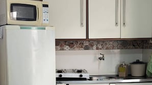 A compact kitchen with white cabinets, a microwave, a stove, and a small sink. - Aconchego Volta Redonda 449 (Volta Redonda)