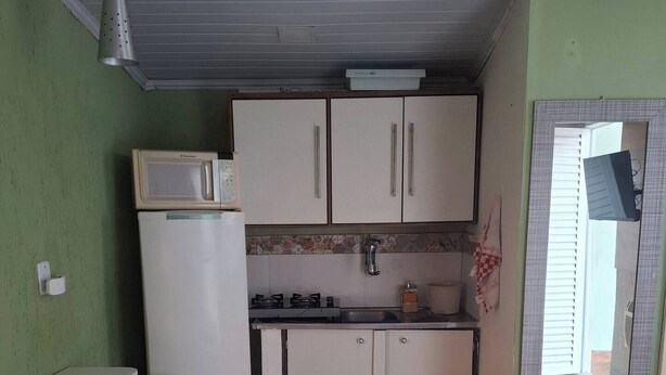 Uma cozinha compacta com armários brancos, micro-ondas, pia e um pequeno espaço de refeições com uma cadeira verde.