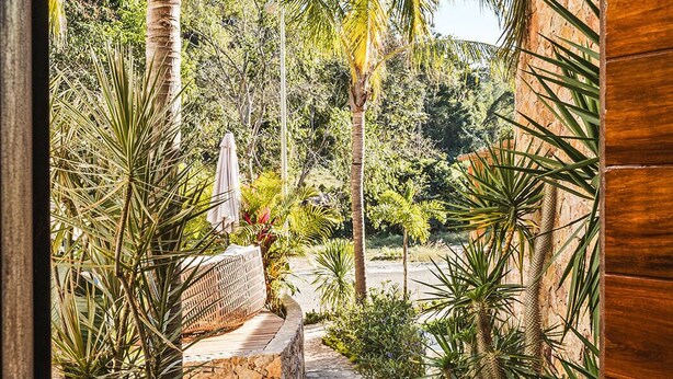 Un vialetto in pietra conduce a un edificio in legno, circondato da rigogliosa vegetazione tropicale e palme.