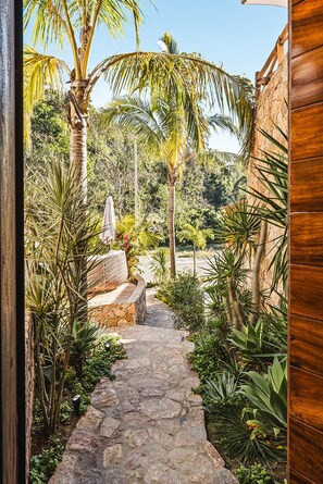Un sendero de piedra conduce a un edificio de madera, rodeado de exuberante vegetación tropical y palmeras.
