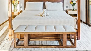 Un letto grande con struttura in legno e una panca a capotesta, soffitto in legno e due lampade da comodino.