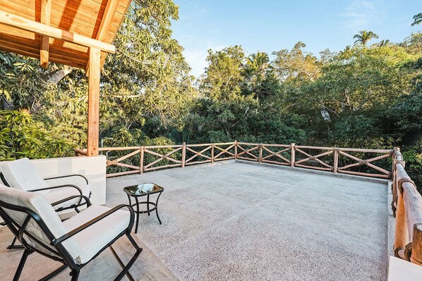 Un patio al aire libre con una pérgola de madera, dos sillones blancos y una mesita.