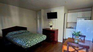 Une petite chambre comprenant un lit, un bureau avec une chaise, une télévision et un coin cuisine.