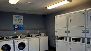 Une buanderie équipée de plusieurs machines à laver et de plusieurs sèche-linge, une affiche faisant la promotion d’une application et un sol carrelé.