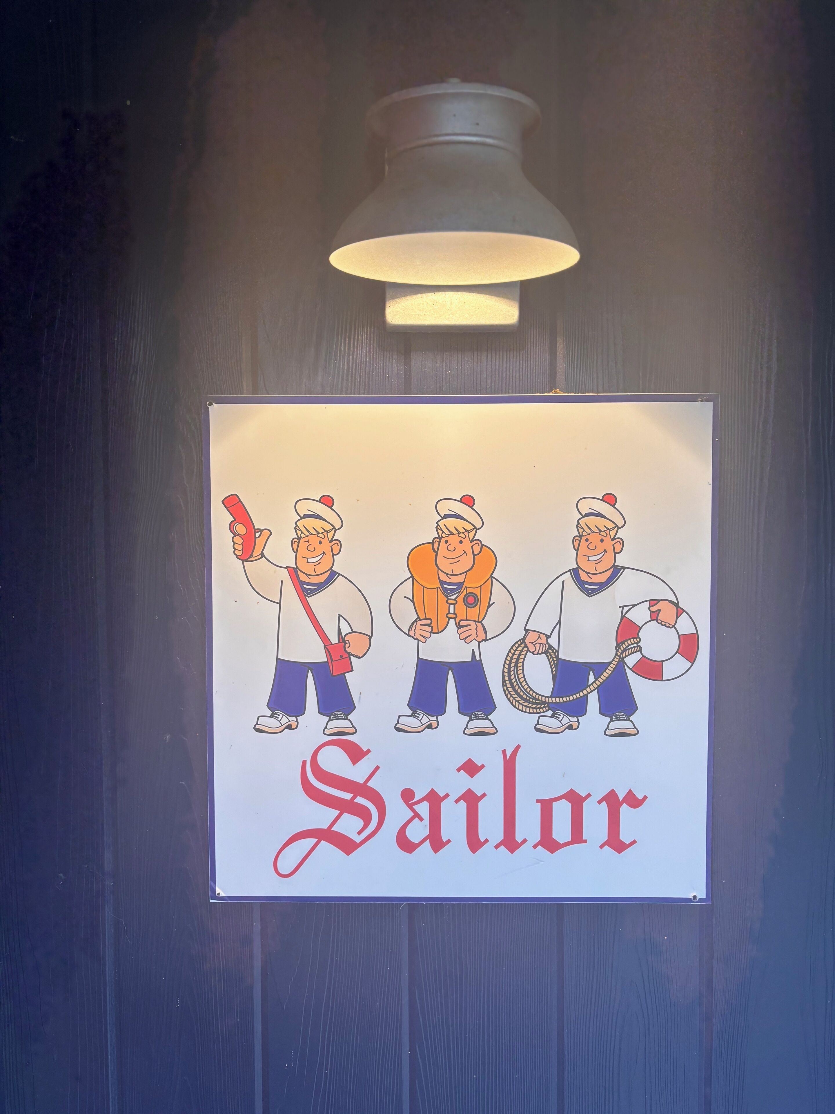 A sign with cartoon sailors and the word "Sailor" on a wooden surface.