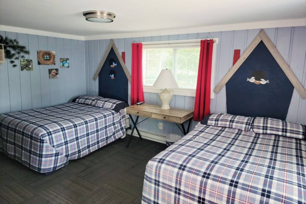 A room with two beds, a desk, and a window with red curtains.
