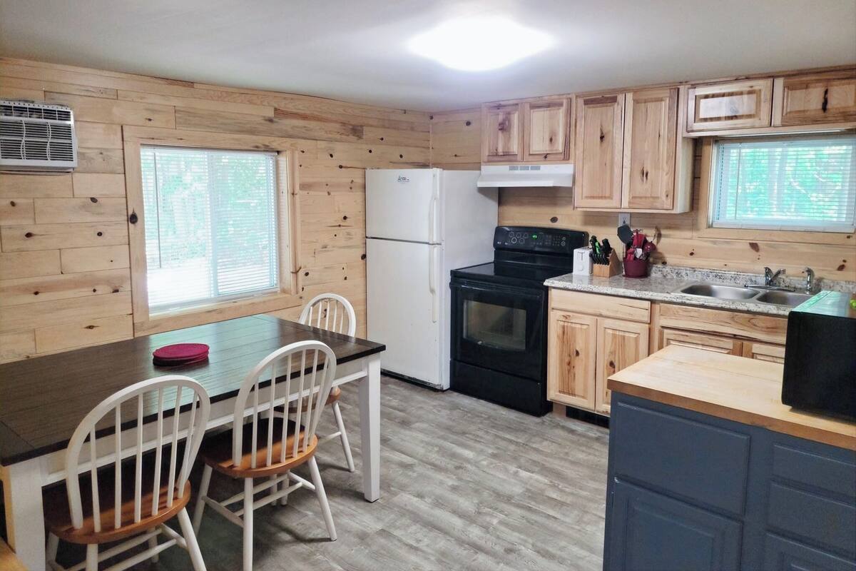 A kitchen with wooden cabinets, a black stove, a white refrigerator, and a dining area with two white chairs.