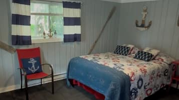 Een slaapkamer met een bed, een stoel, een raam met gordijnen, een plafondlamp en een decoratieve ankerafbeelding aan de muur.