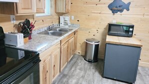 Eine kleine Küche mit Holzausstattung, einem doppelten Spülbecken, einer Mikrowelle, einer Kaffeemaschine und einem Mülleimer.
