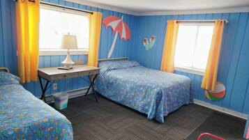 Une chambre avec deux lits, un bureau et une chaise. Les fenêtres sont dotées de rideaux, et un élément décoratif sur le thème de la plage orne le mur.
