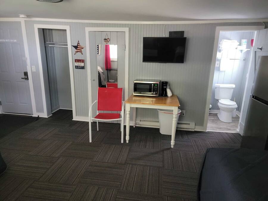 A compact living space with a kitchenette, a dining area with a red chair, and a TV mounted on the wall.