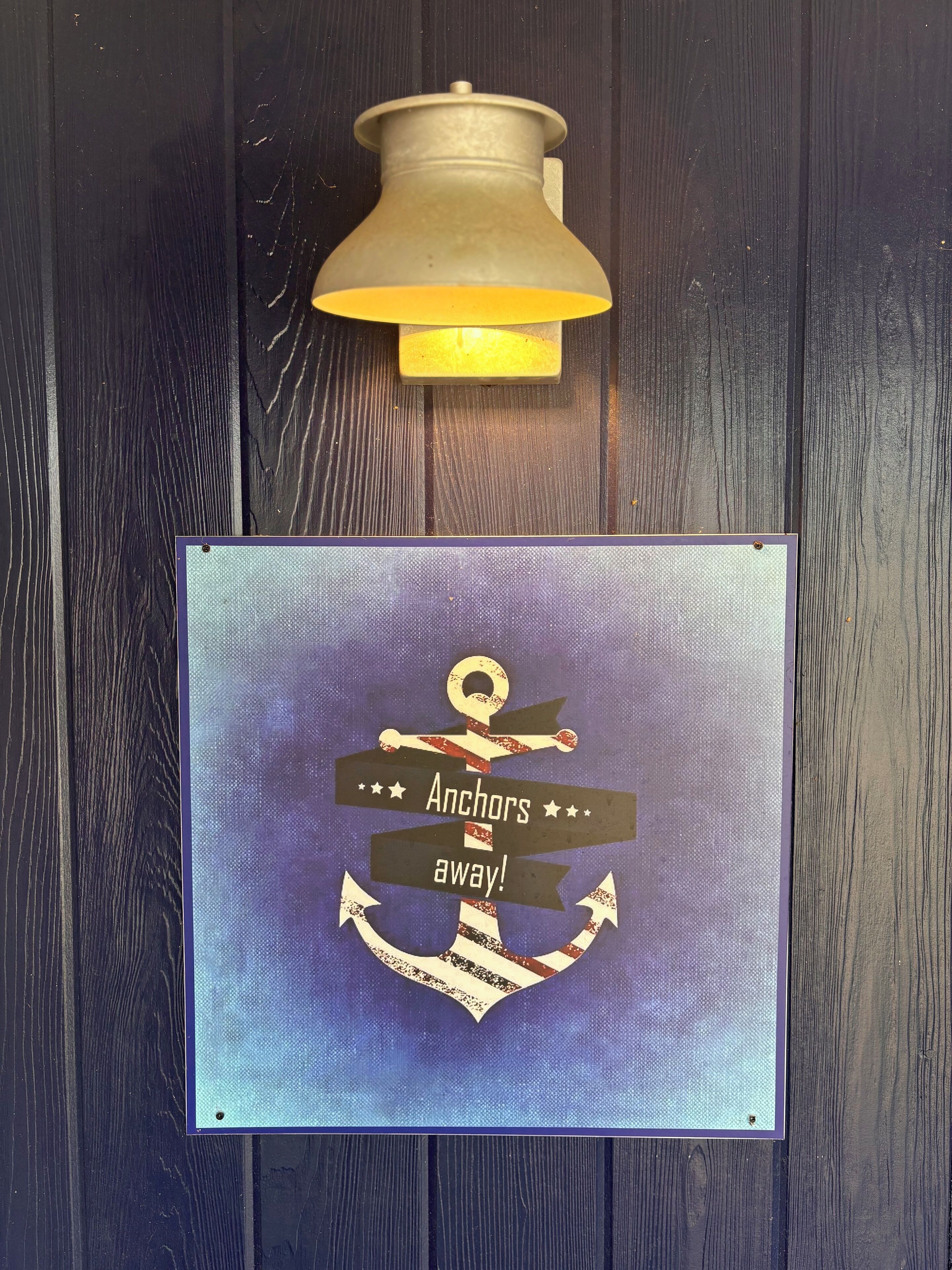 A wall-mounted light fixture and a framed sign with an anchor design and the text "Anchors away!"
