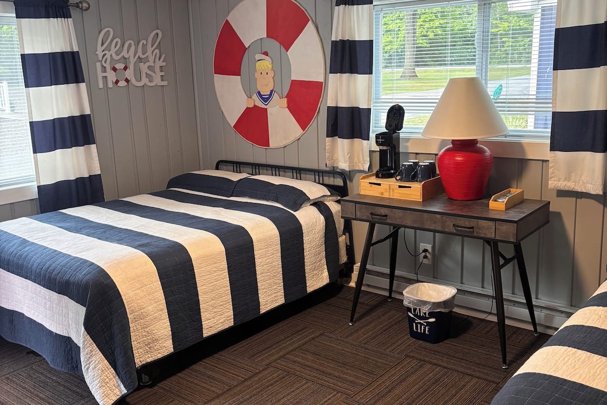A room with a bed, a desk, a lamp, and a trash bin.